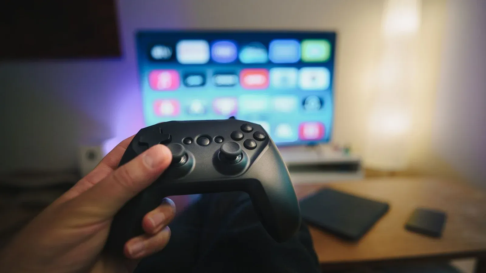 Close-up of a person holding a gaming controller in a cozy living room setup with TV.