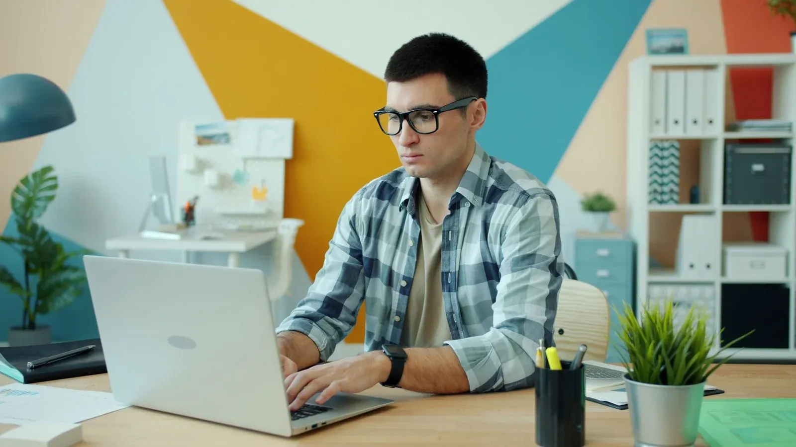 Young adult man working on a laptop in a modern office with colorful decor.