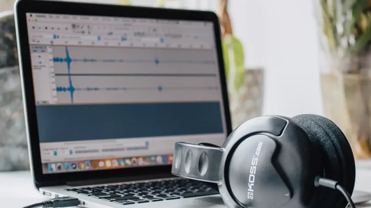 Primer plano de una computadora portátil con software de edición de audio y auriculares en un entorno de oficina en casa.