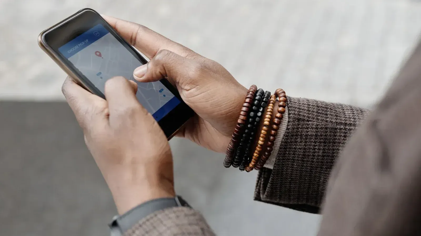 Close-up de manos con pulseras navegando en smartphone usando la aplicación GPS al aire libre.