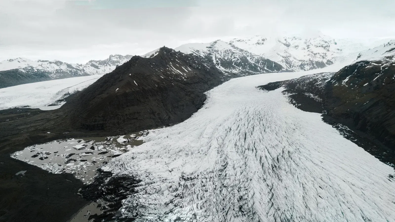 Stunning aerial view of a vast glacier surrounded by snow-capped mountains and icy terrain.