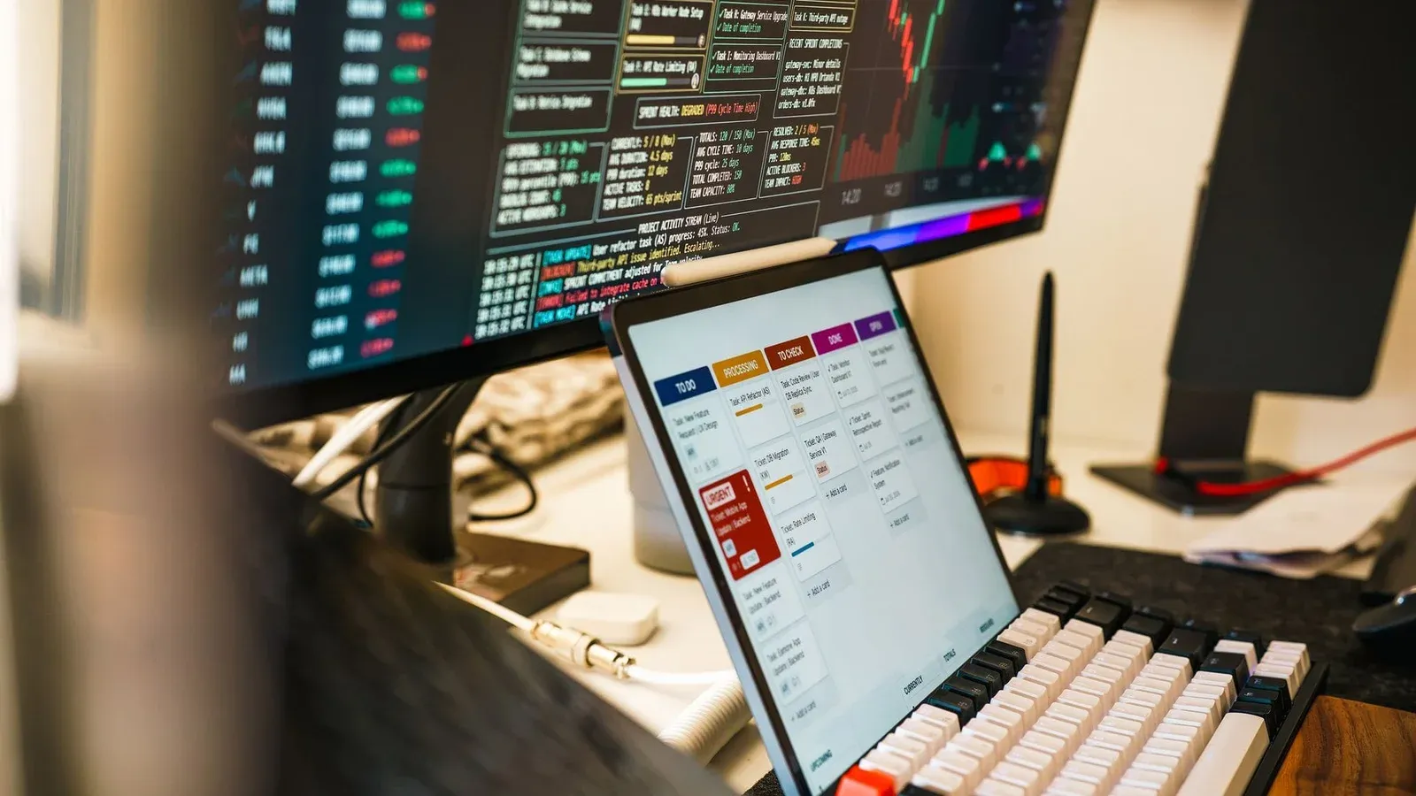 A sleek, modern workspace featuring trading monitors and a tablet for project management.