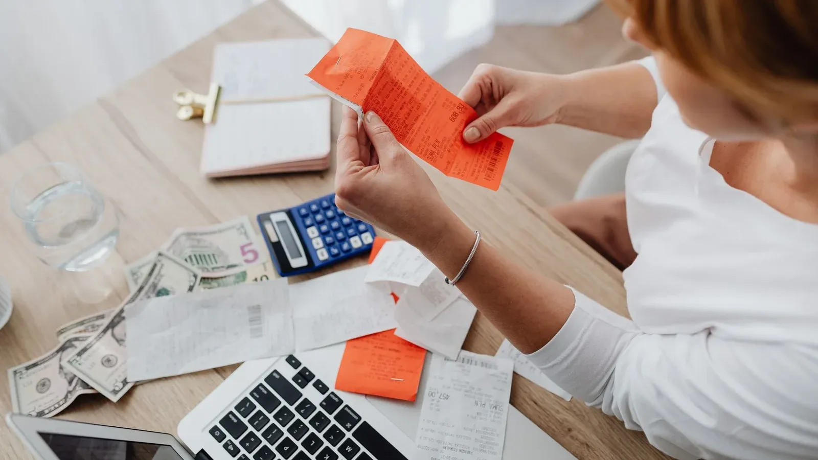 Woman using calculator and receipts at home office desk for finance management.