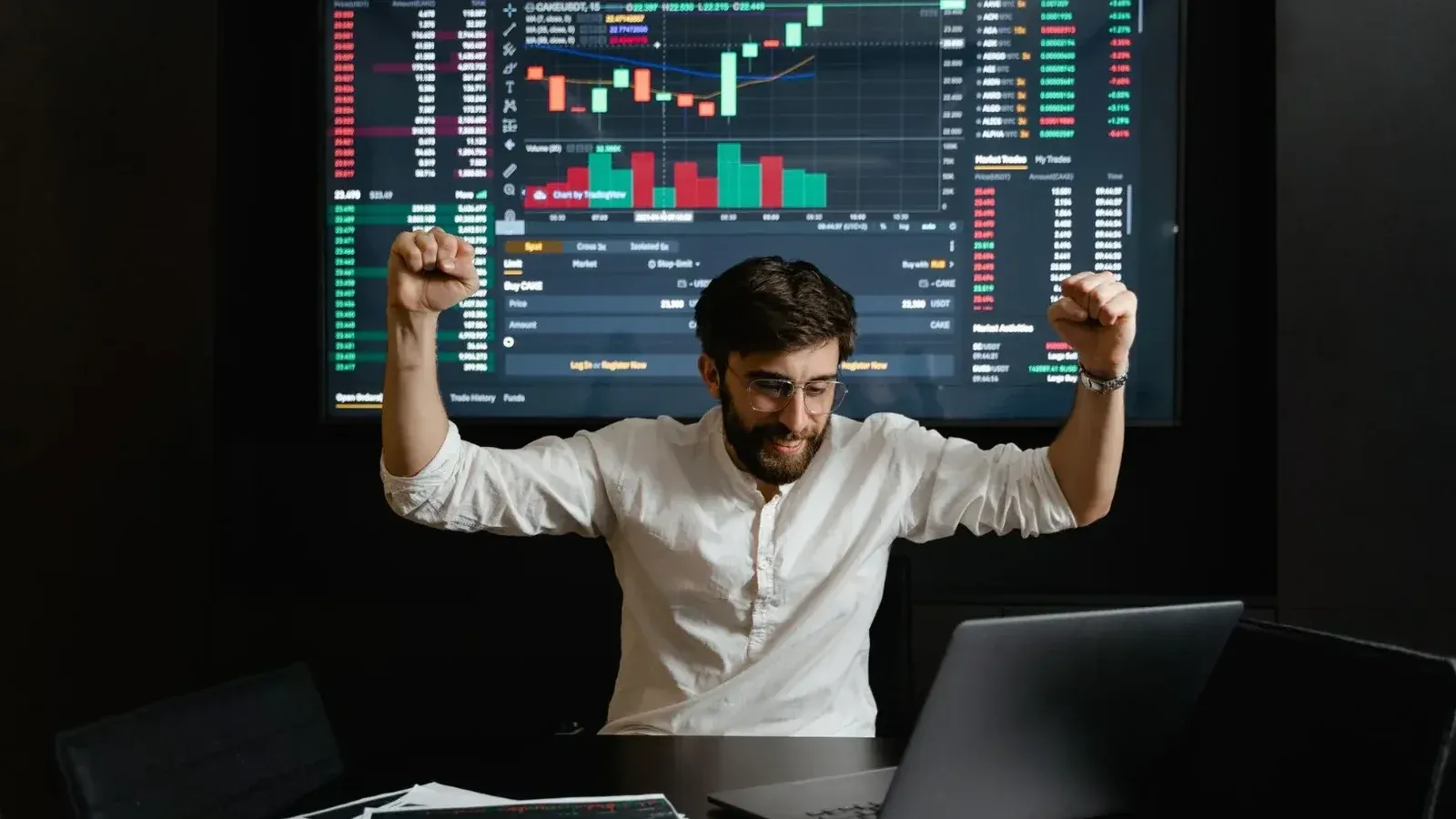 El empresario celebra el éxito del mercado de valores con las manos levantadas de emoción en una mesa de negociación.