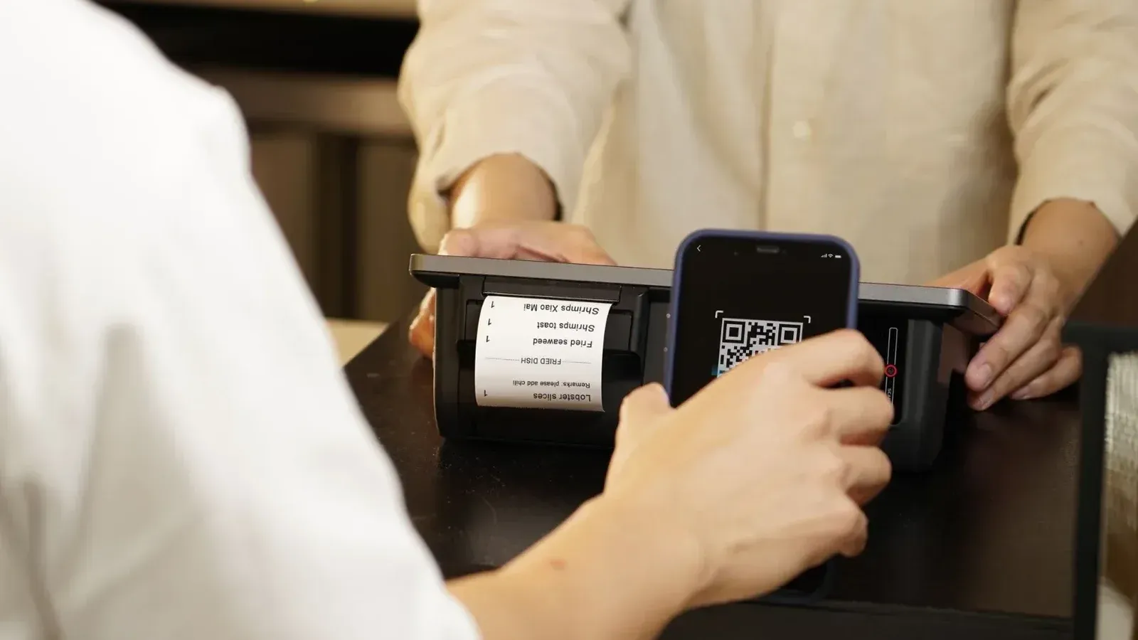 Two individuals engaged in a contactless payment using a QR code scanner at a retail counter.