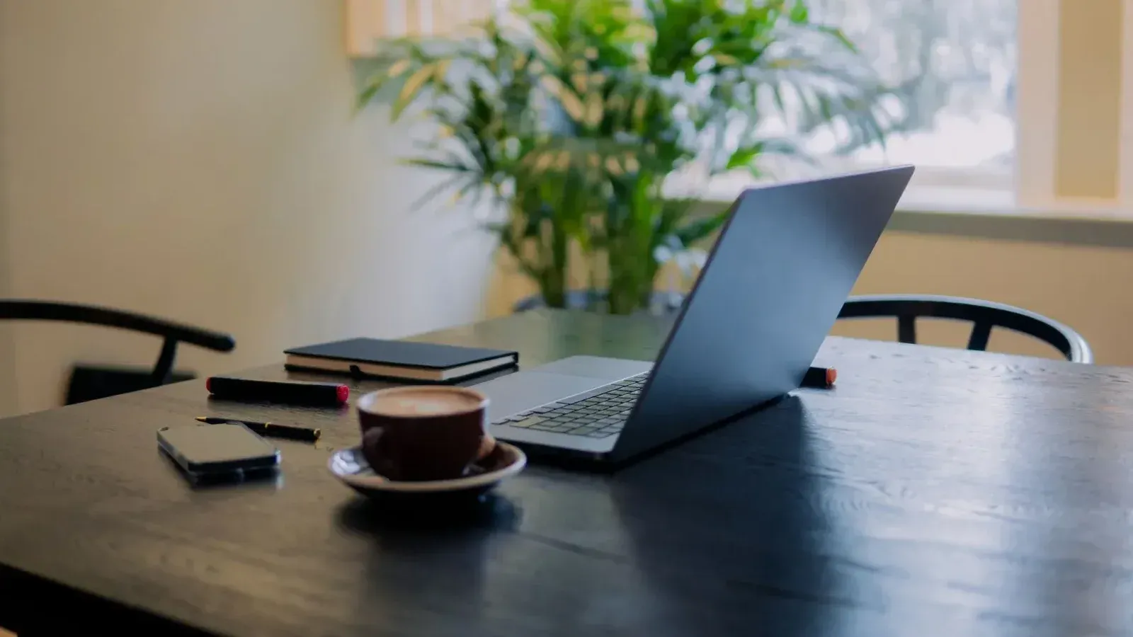Un espacio de trabajo cálido y acogedor en Ámsterdam con una computadora portátil, café y una planta en maceta.