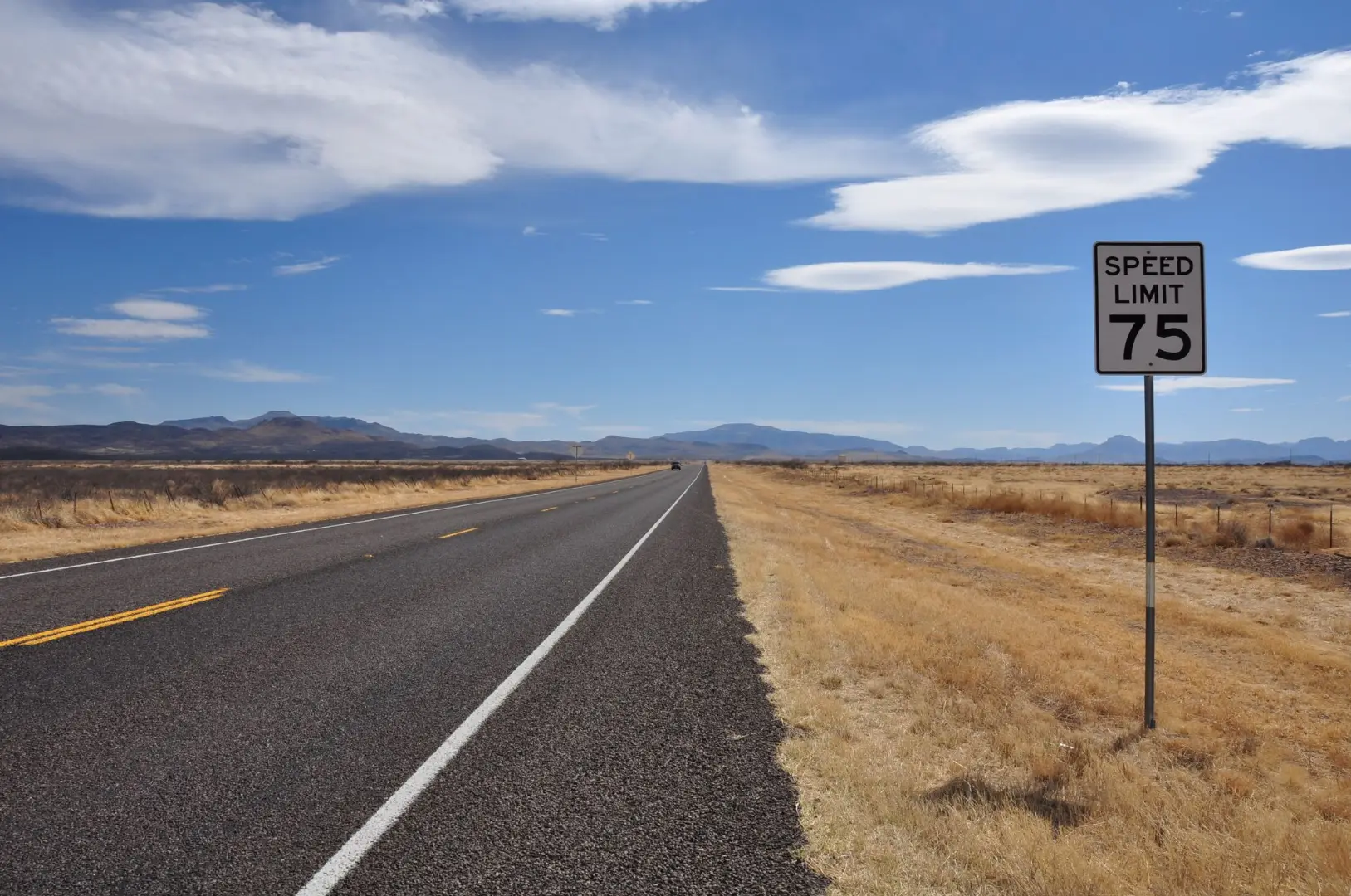 A deserted highway stretches into the horizon under a bright blue sky with a speed limit sign in the countryside.