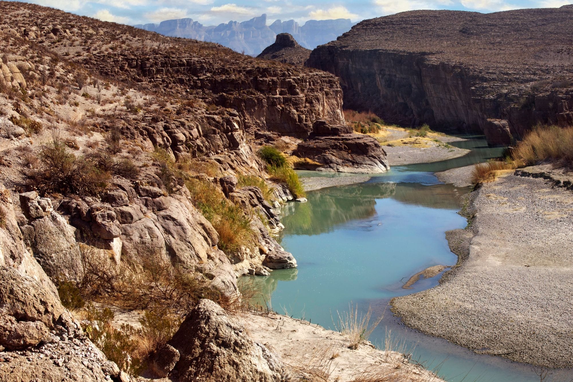 Stunning view of a canyon with turquoise river winding through arid landscape, framed by rugged rocky cliffs.