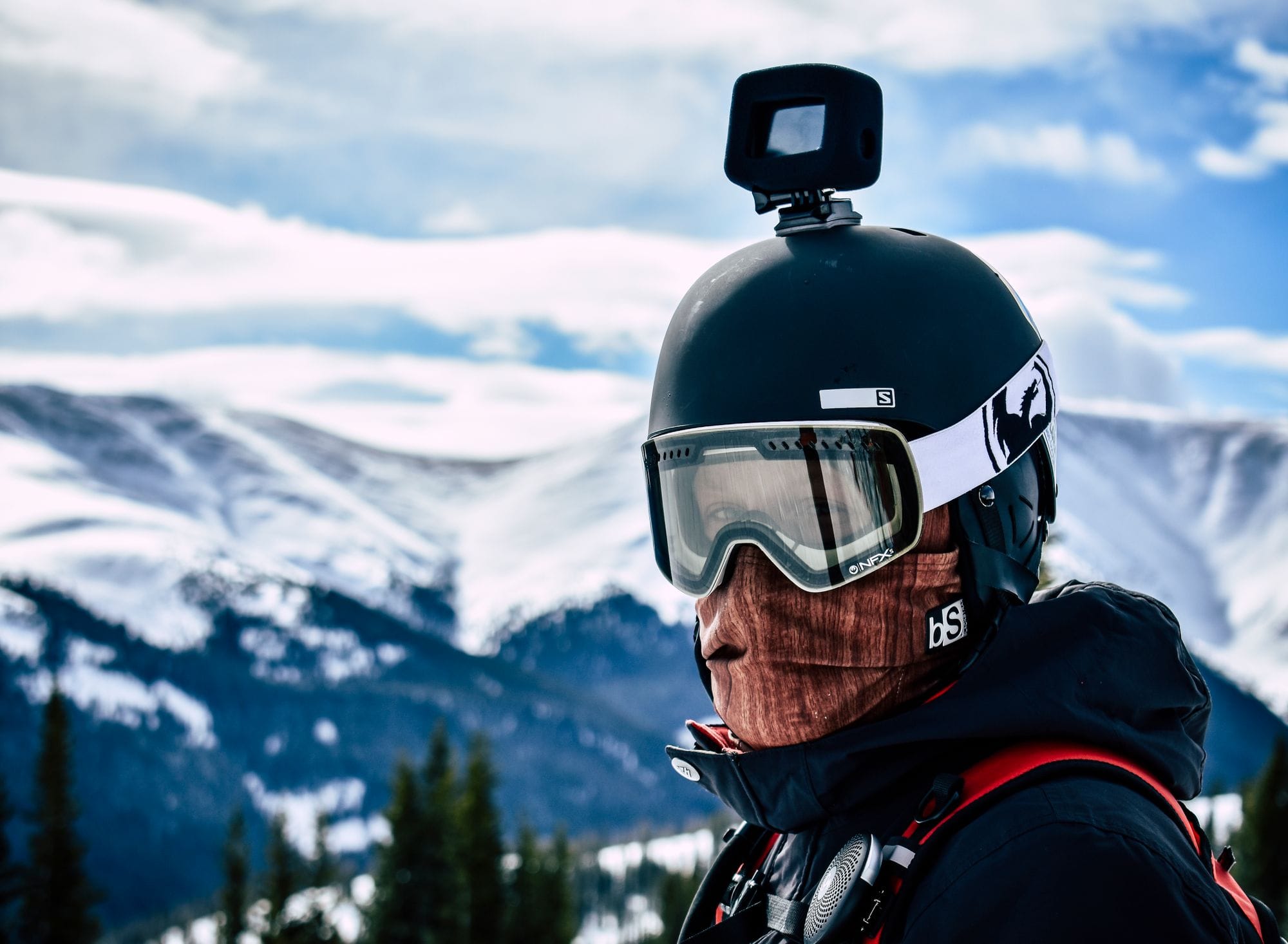 Close-up of a skier with helmet camera in snowy mountain landscape, showcasing winter sports adventure.