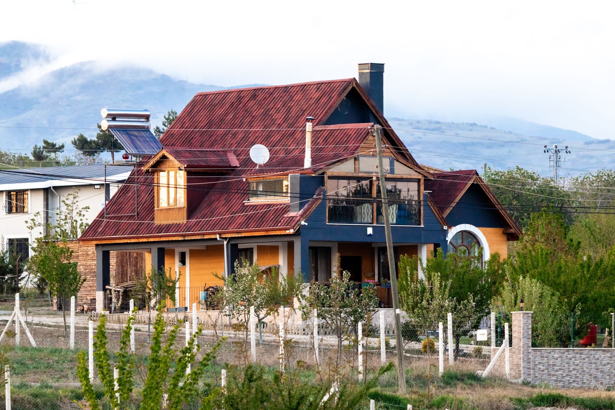 A picturesque house with a red roof surrounded by lush greenery at the base of scenic mountains.