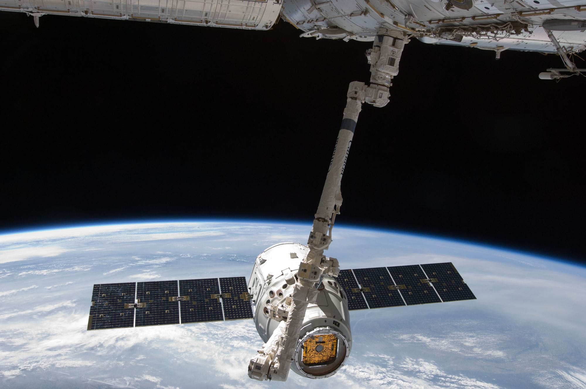 View of a spacecraft docked at the ISS above Earth with visible solar panels.