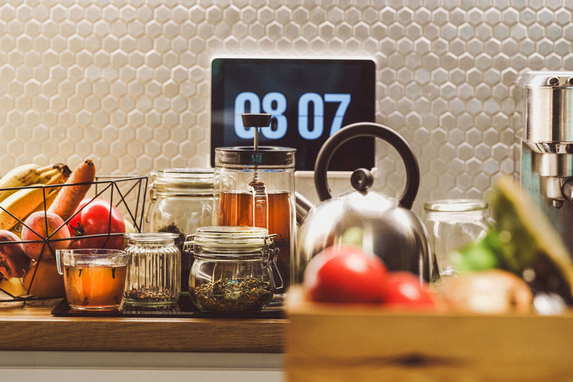A cozy kitchen counter with tea, fruits, and digital clock creating a warm domestic ambiance.