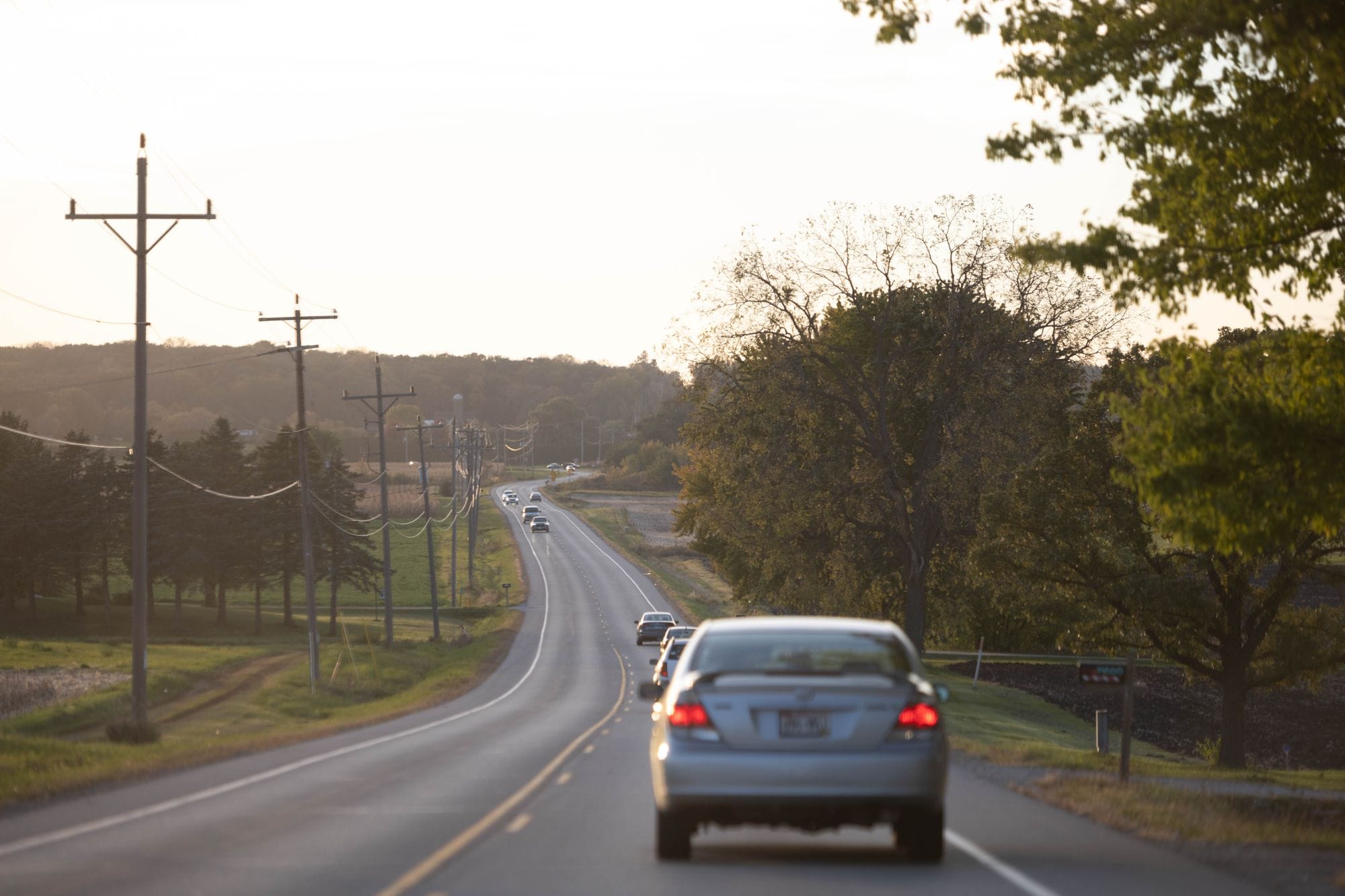 Cars driving on a peaceful rural road in Spring Grove, Illinois at sunset, surrounded by nature.