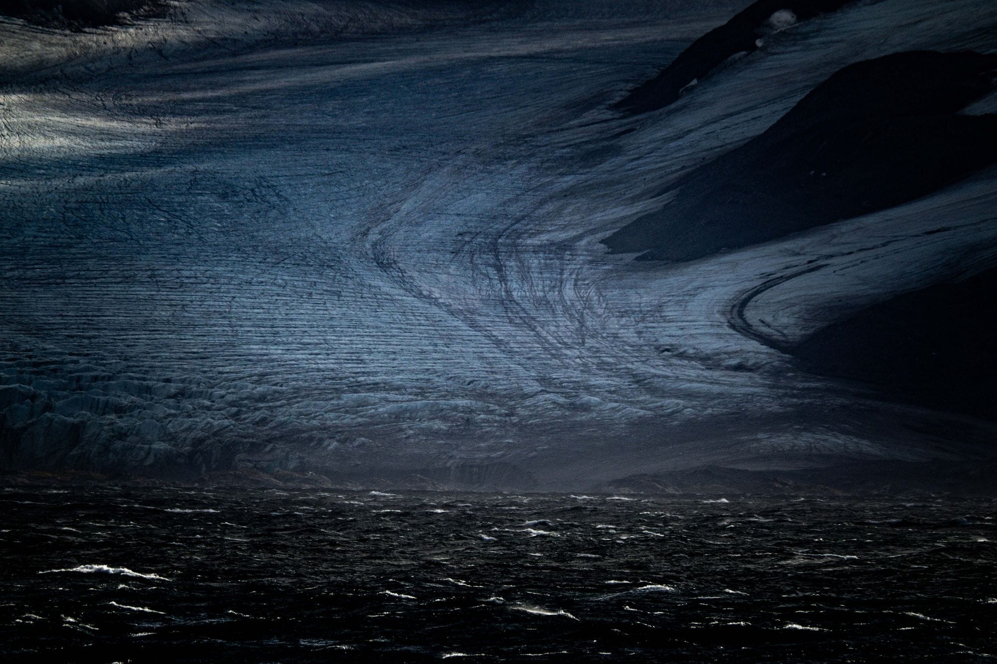 A stunning dark glacier meeting the ocean, captured in low light for dramatic effect.