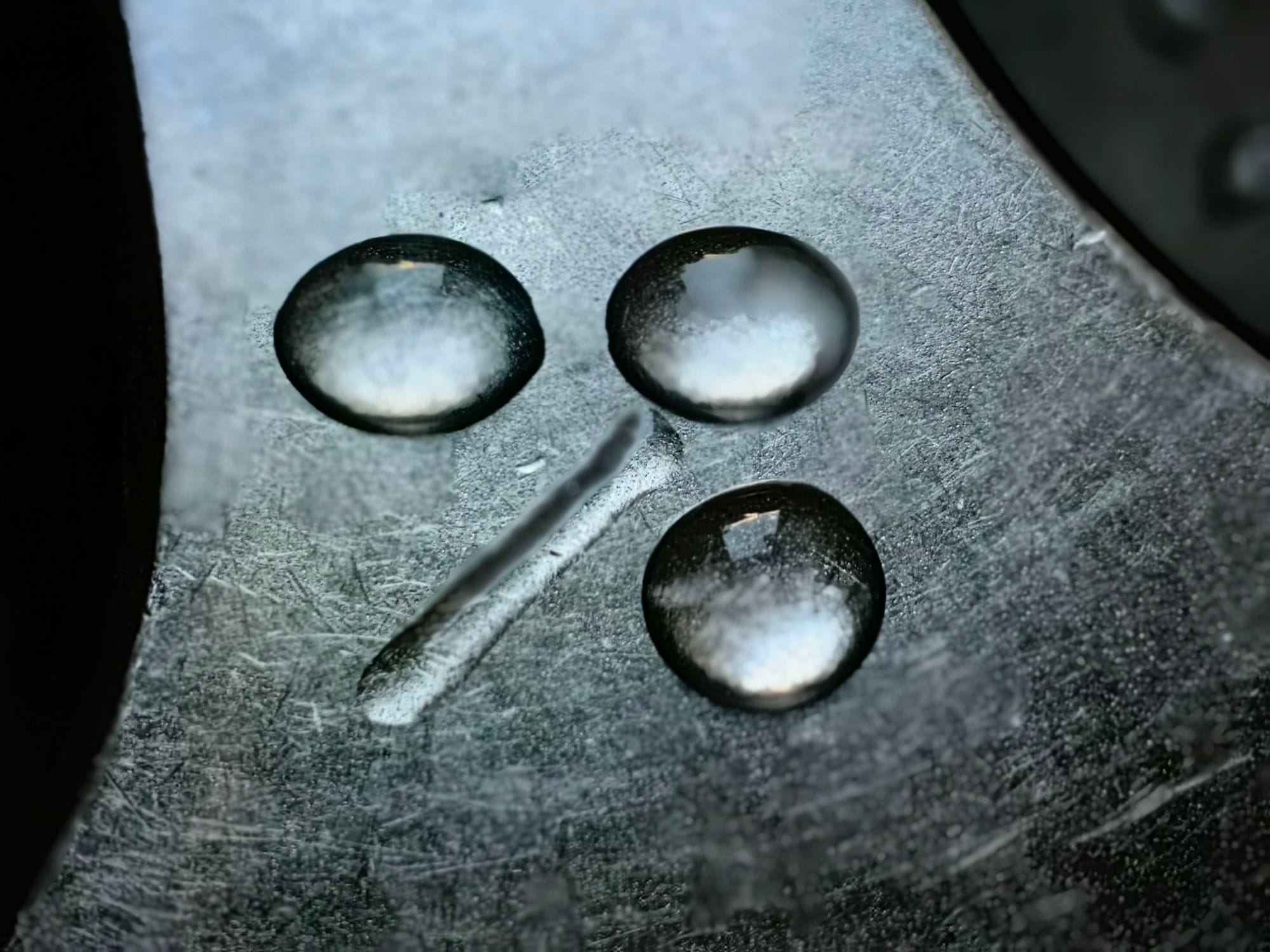 Detailed macro shot of water droplets on textured metal surface. High contrast and reflective detail.