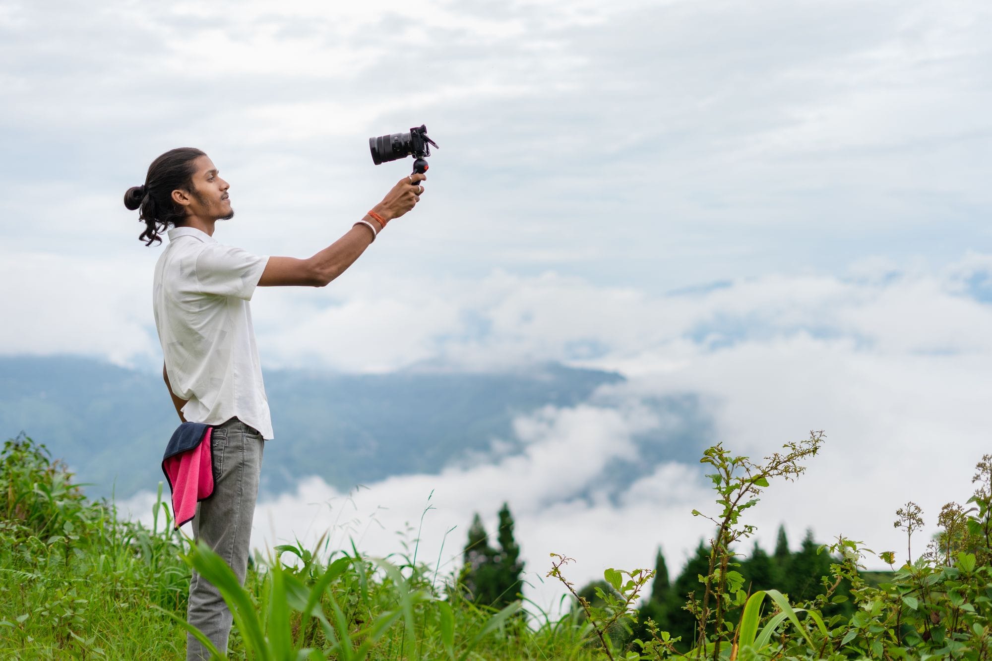A young man films a lush, misty mountain landscape on an overcast day, capturing nature's beauty.