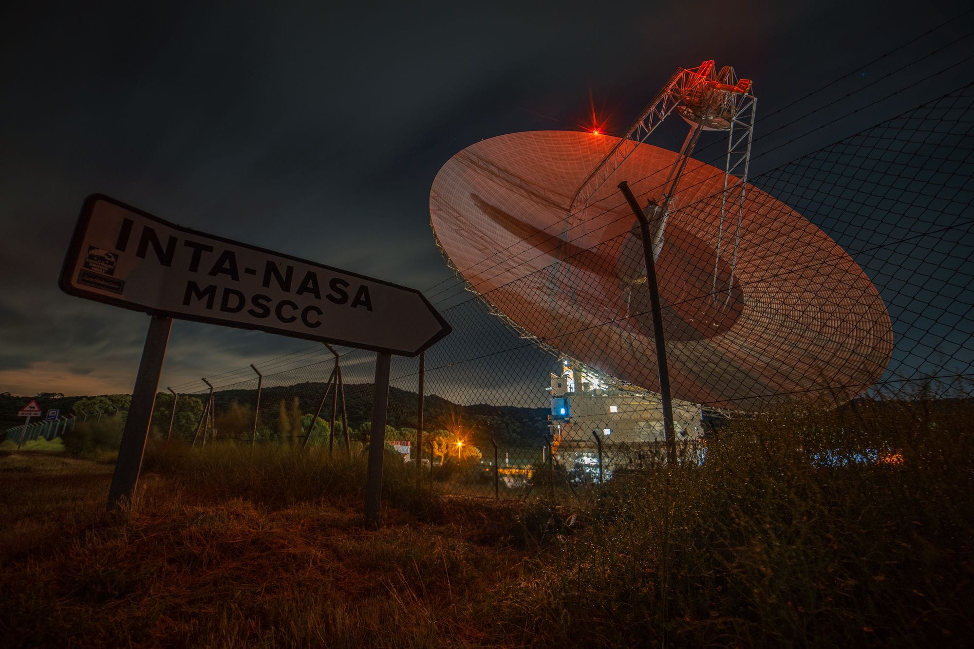 A nighttime view of a satellite dish at Madrid Deep Space Communications Complex under a dark sky.