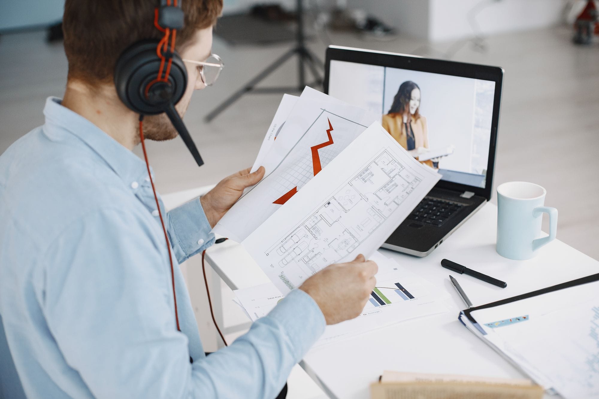 Man with headphones reviews charts while working remotely at desk.