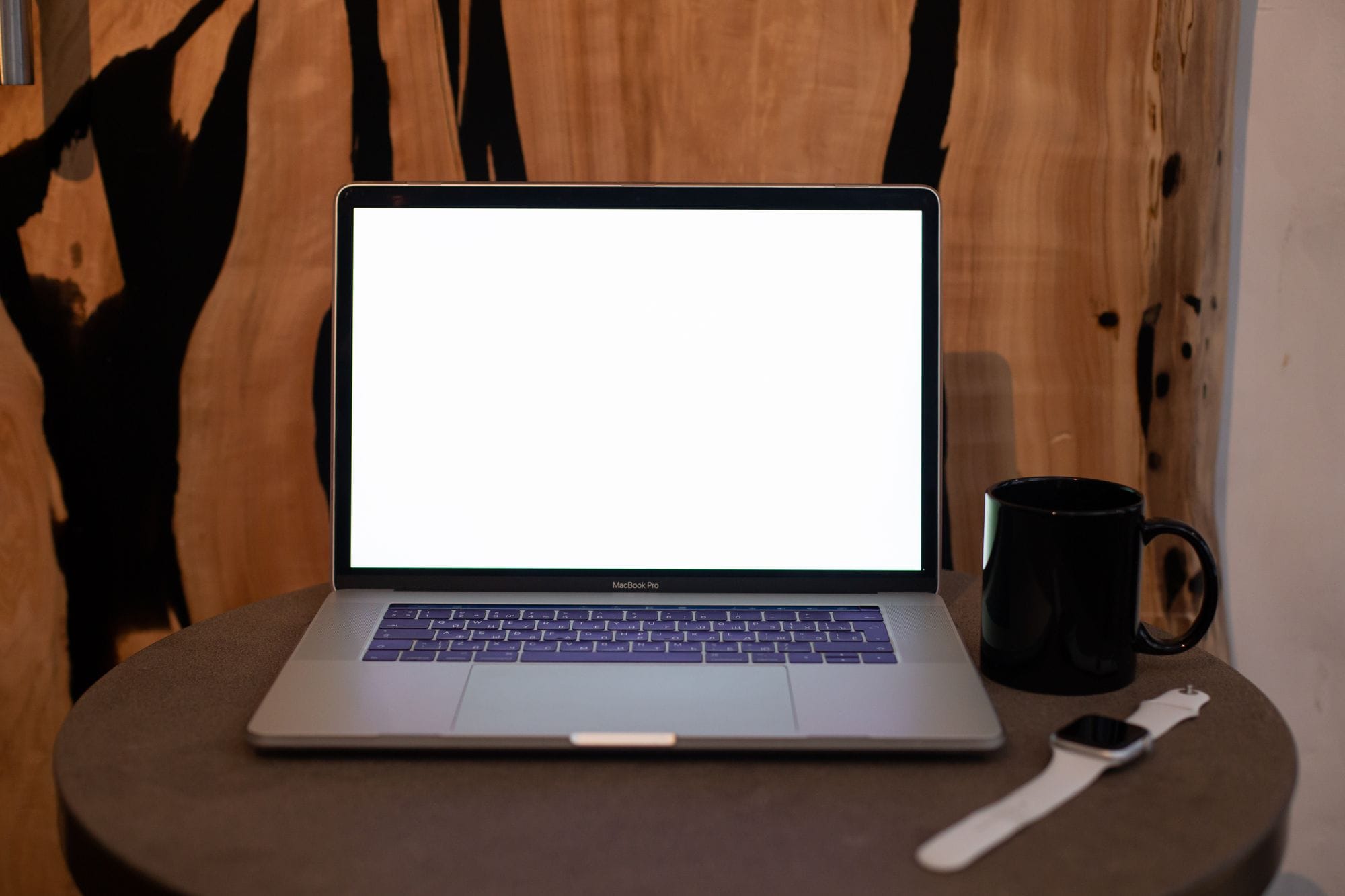 A contemporary workspace featuring a laptop with blank screen, coffee mug, and smartwatch on a table.