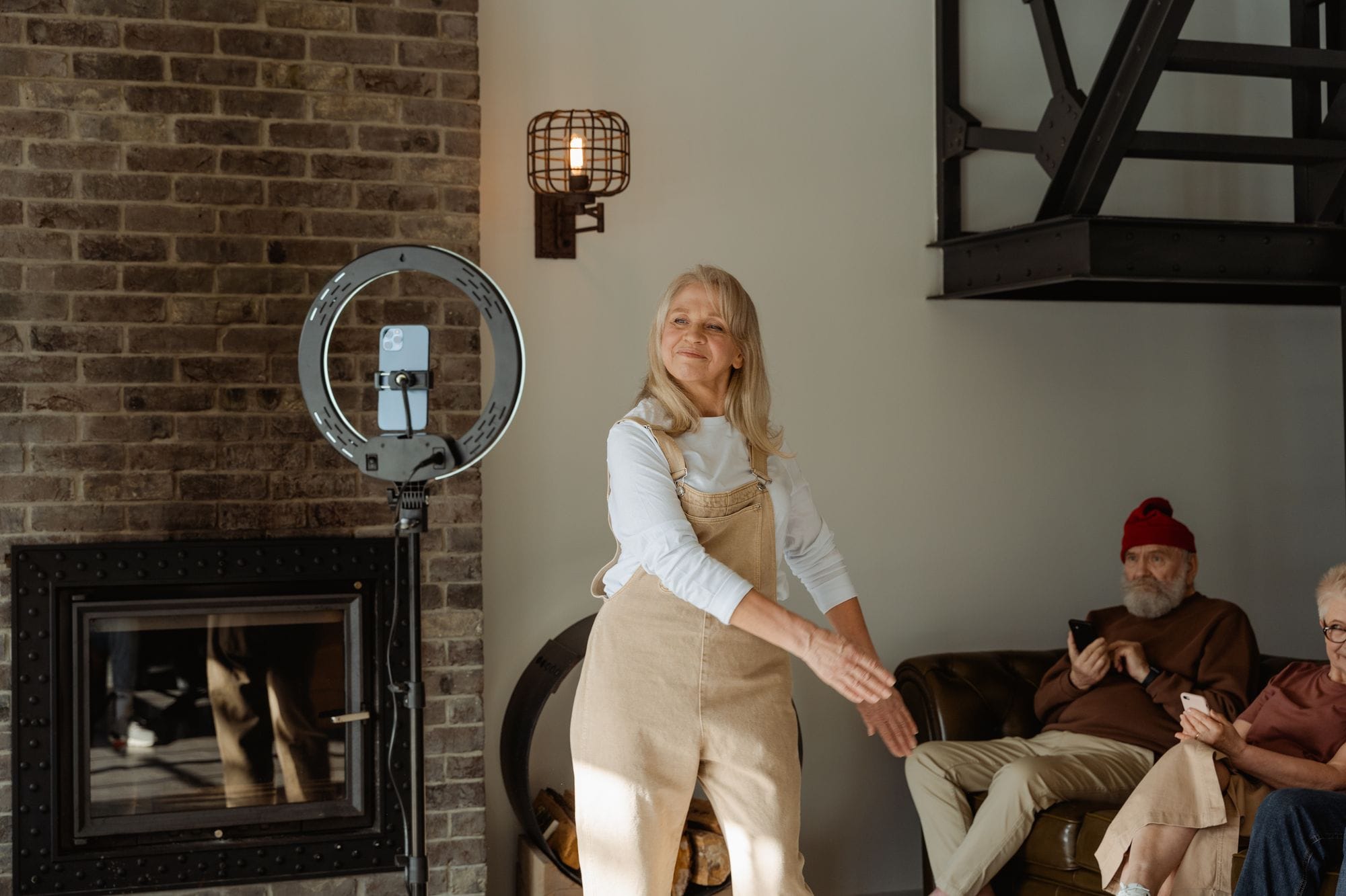 Cheerful senior woman dancing by a fireplace indoors, accompanied by friends.