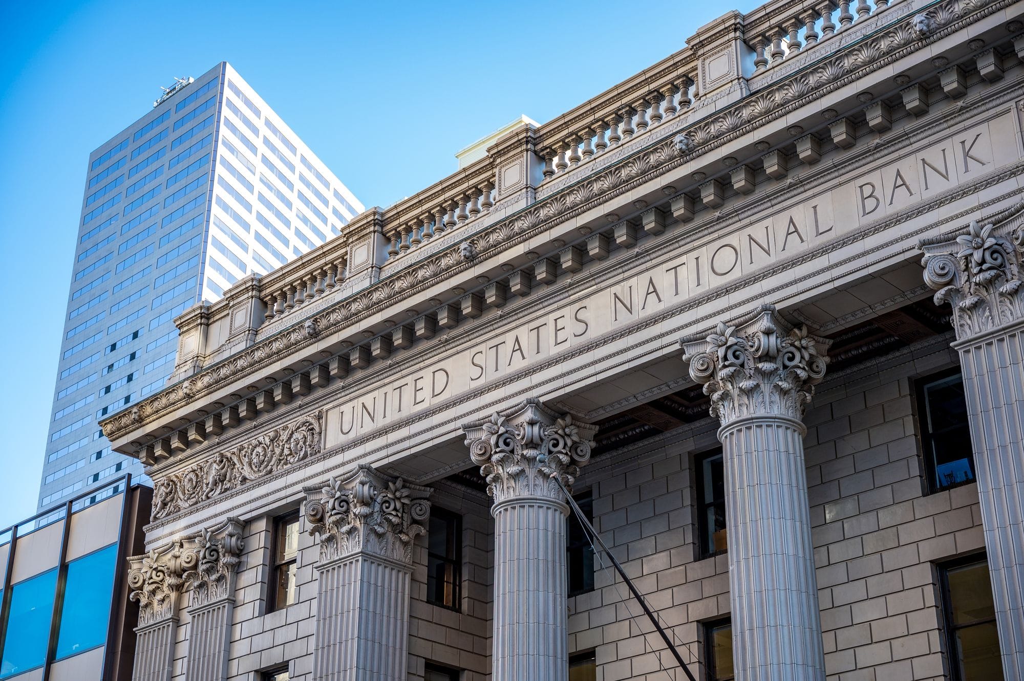 Exterior of historic national bank with decorative elements on classic columns located in city with modern building against blue sky