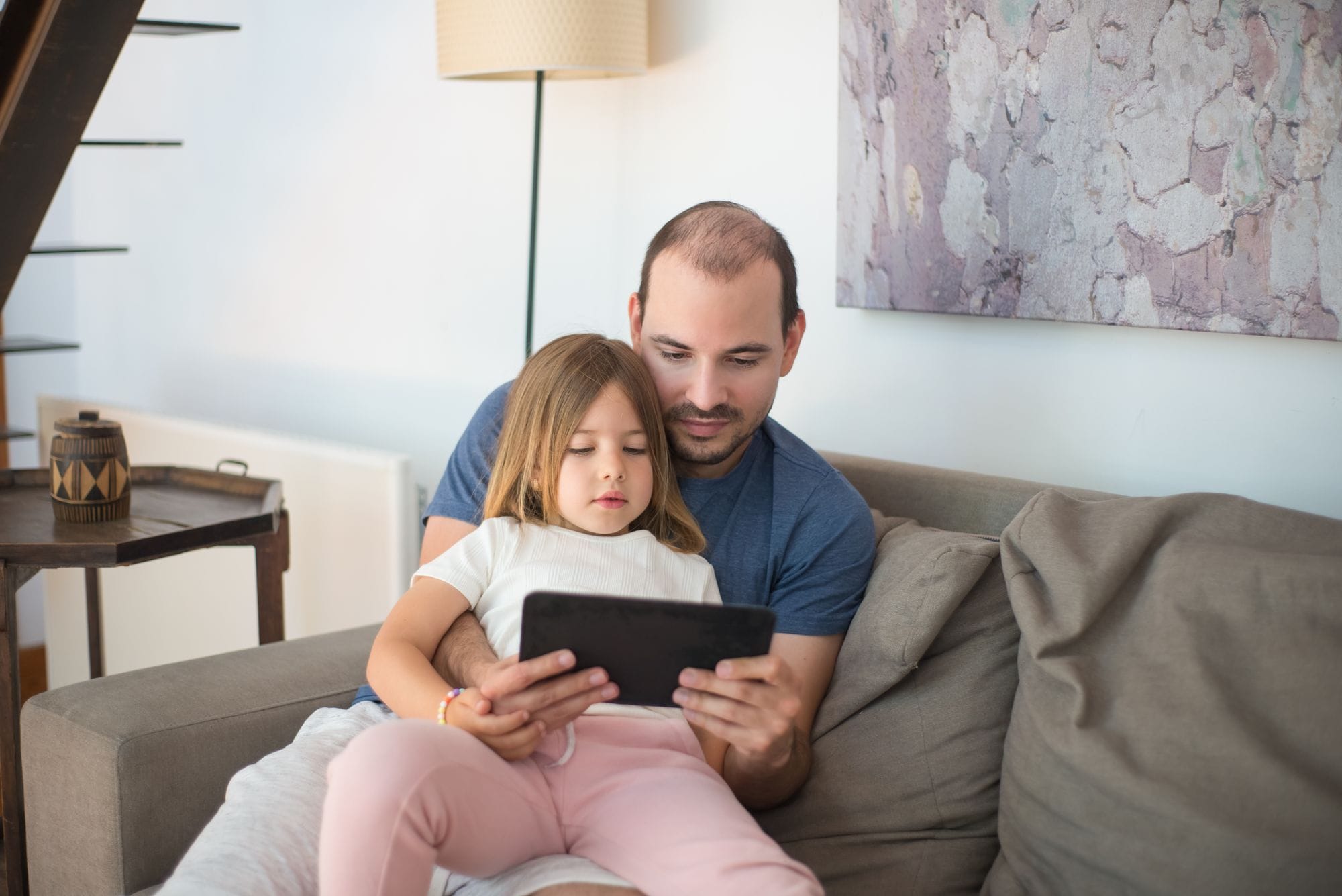 A father and daughter enjoying quality bonding time together on a couch using a tablet.