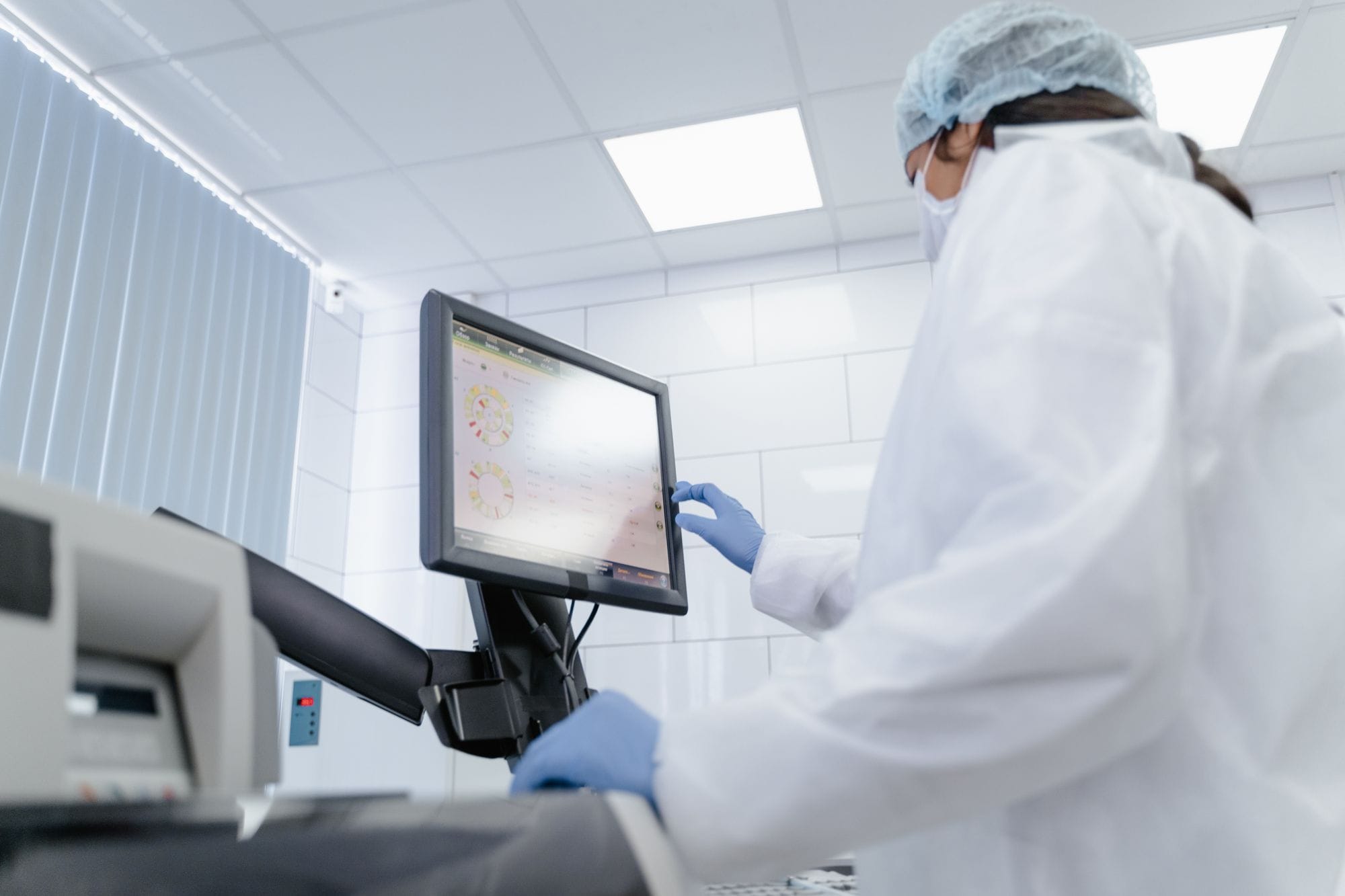 Woman in lab coat using touchscreen monitor in a modern laboratory setting.