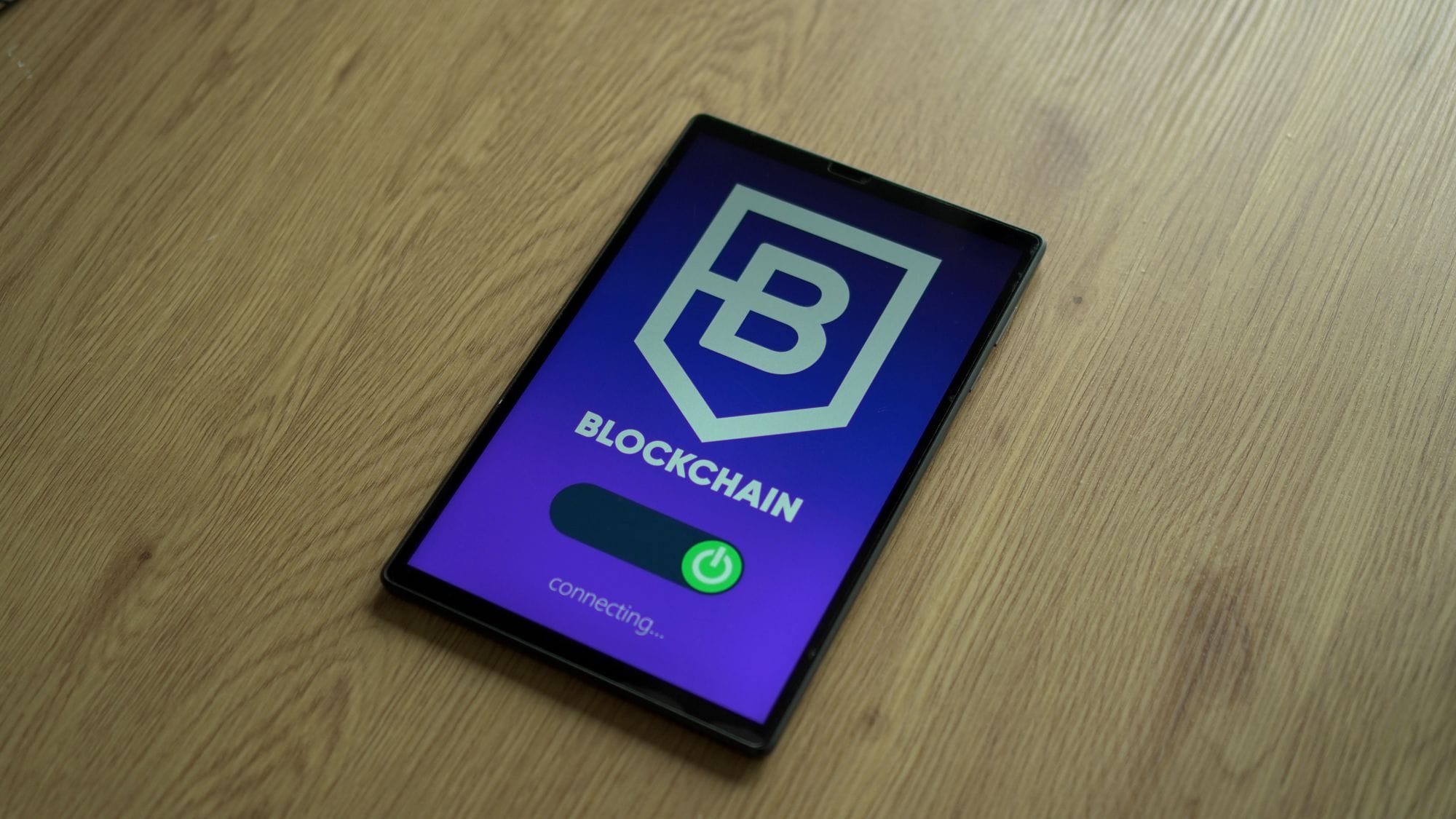 Close-up of a digital tablet showing a blockchain concept screen on a wooden surface.