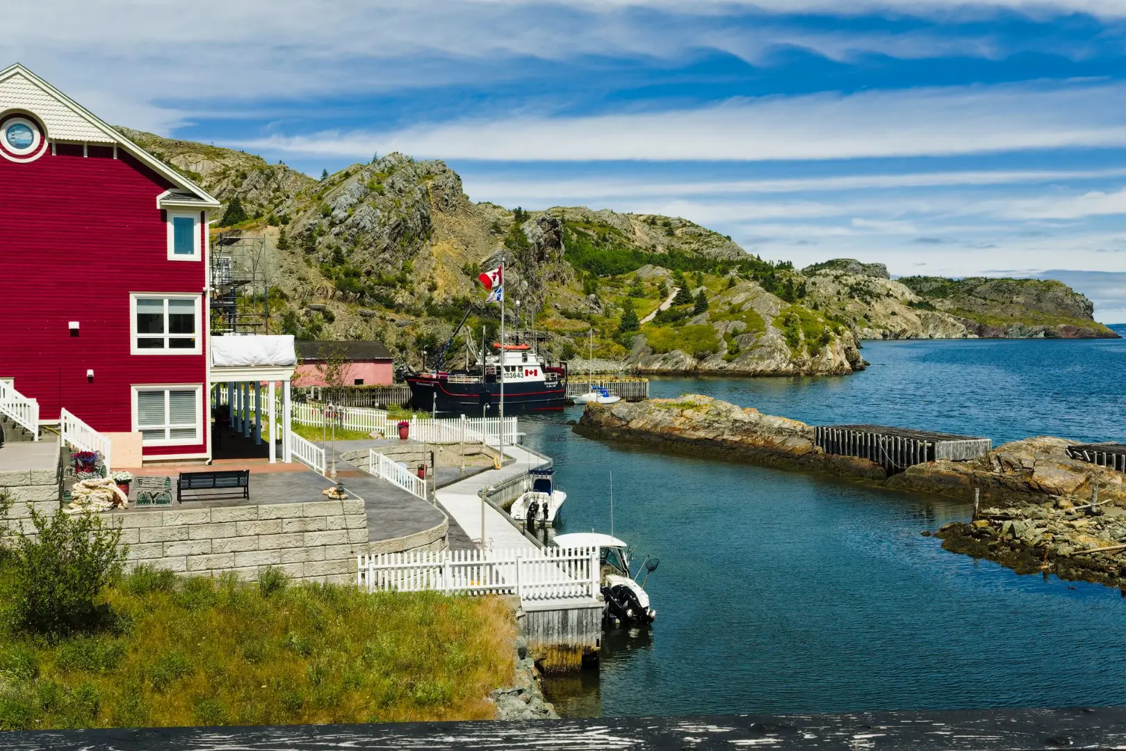 Picturesque harbor scene in Brigus, Newfoundland with a vibrant red house and docked boat.