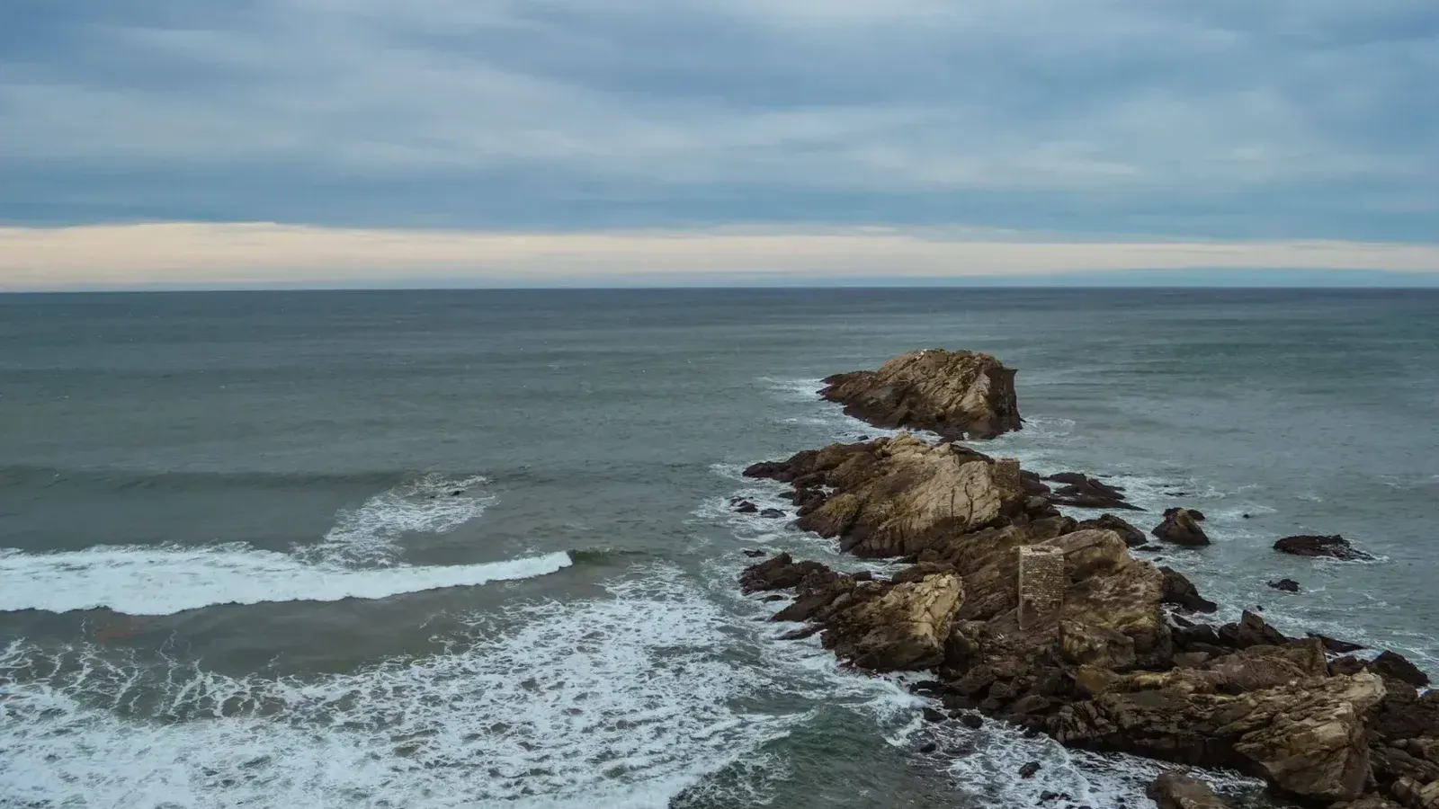 Captura de rocas y olas escarpadas en la playa de Zarautz en un día nublado.