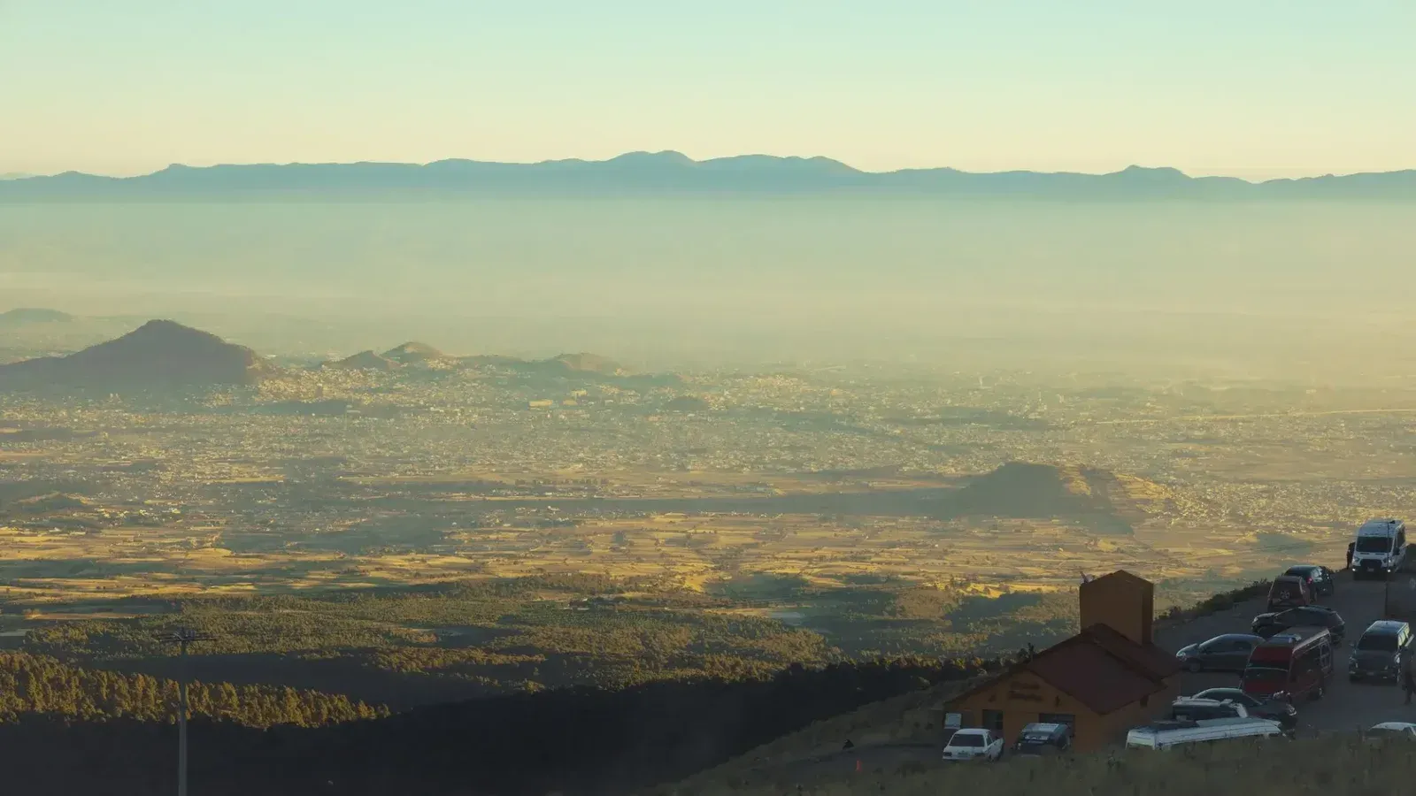 Aerial view of a city in a valley, with smog and distant mountains creating a serene landscape.
