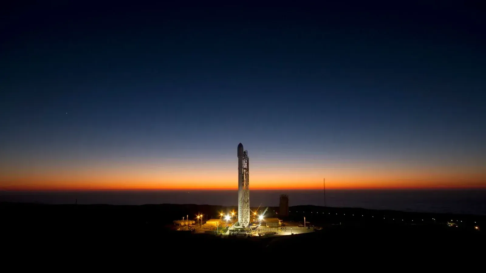 A powerful rocket stands ready on its launch pad against a stunning twilight sky.
