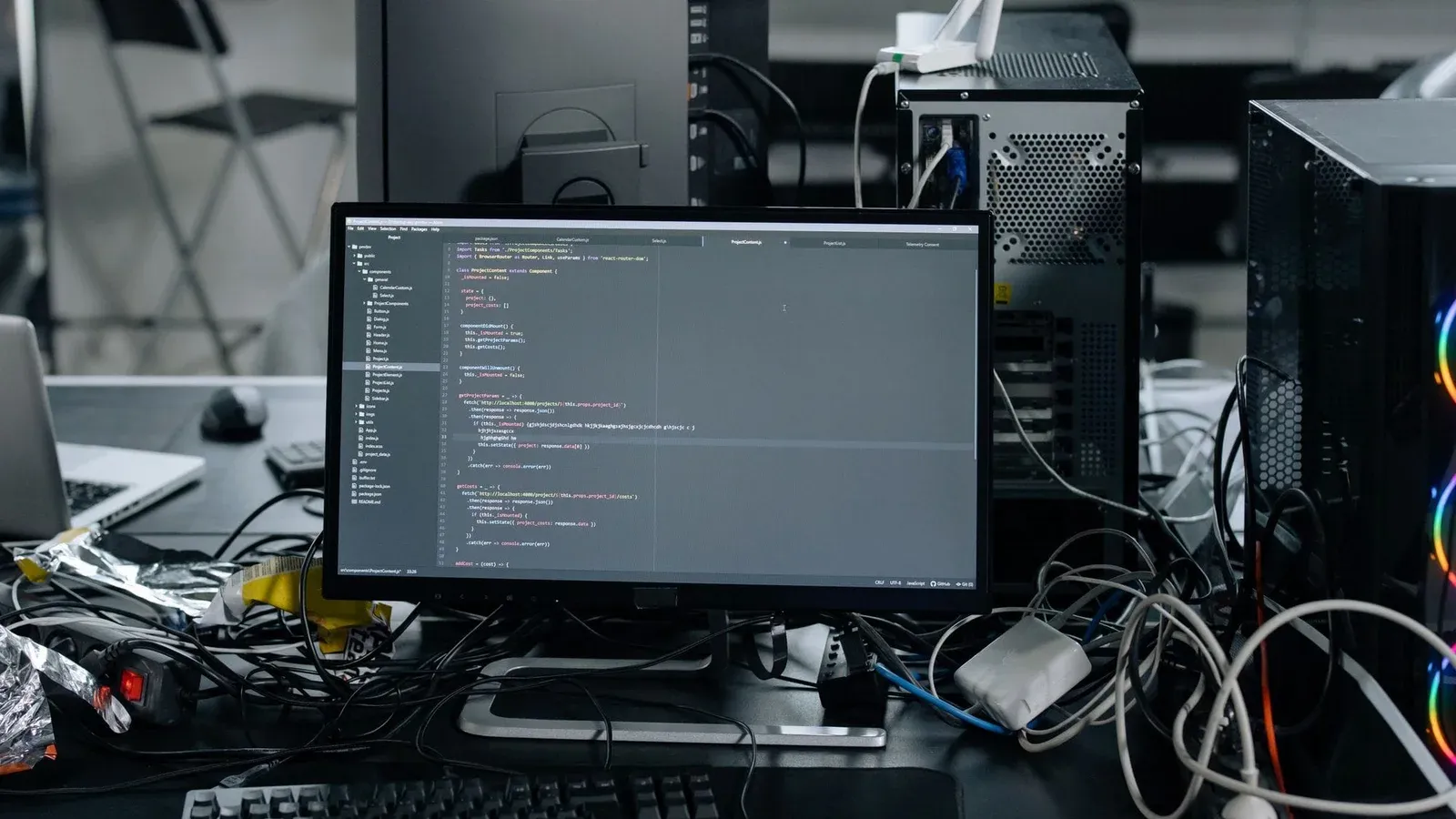 A cluttered workstation in an office featuring a monitor displaying code, surrounded by a keyboard, mouse, and wiring.