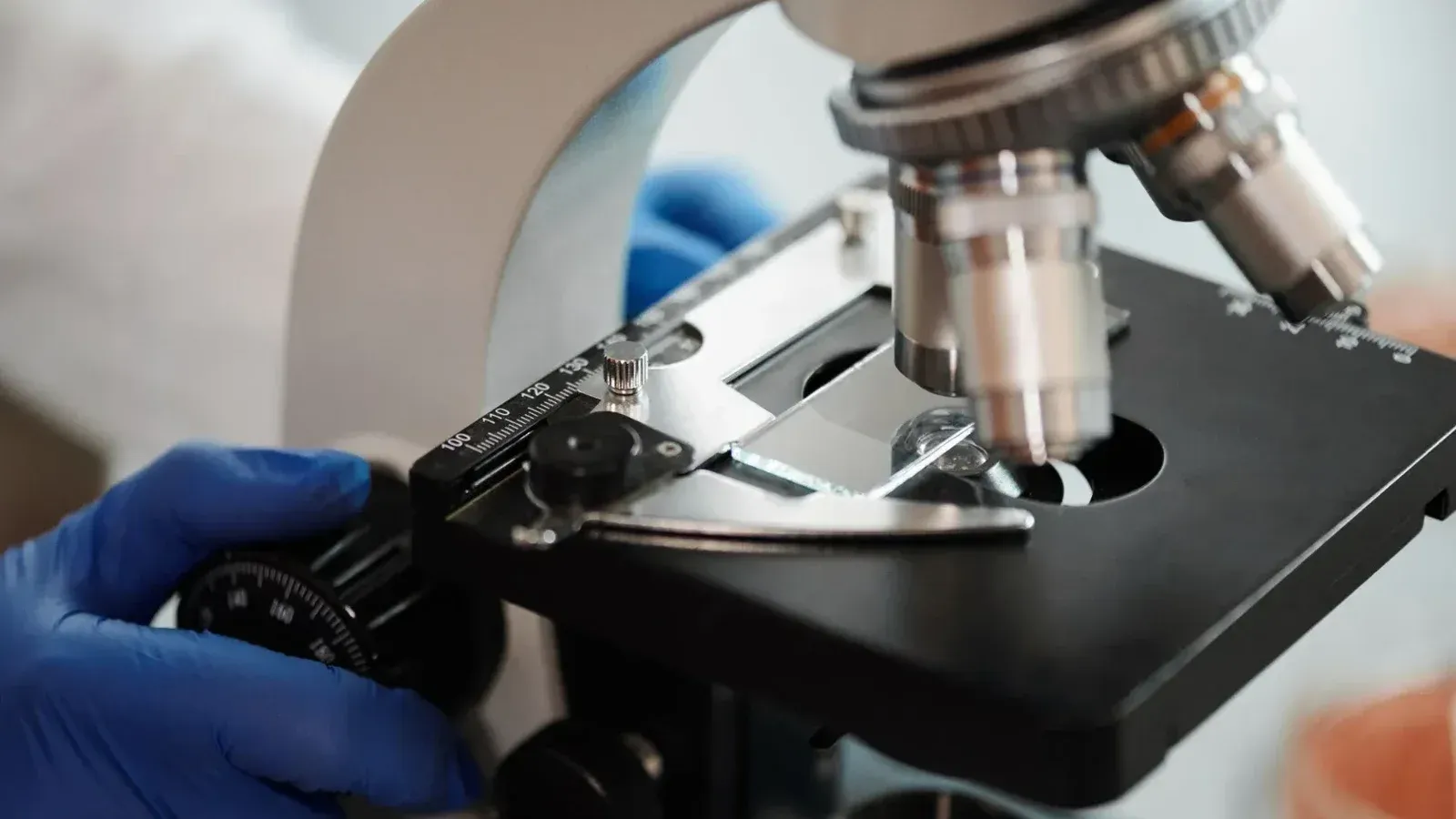 Imagen de primer plano de la mano enguantada de un científico ajustando un microscopio en un laboratorio de investigación.