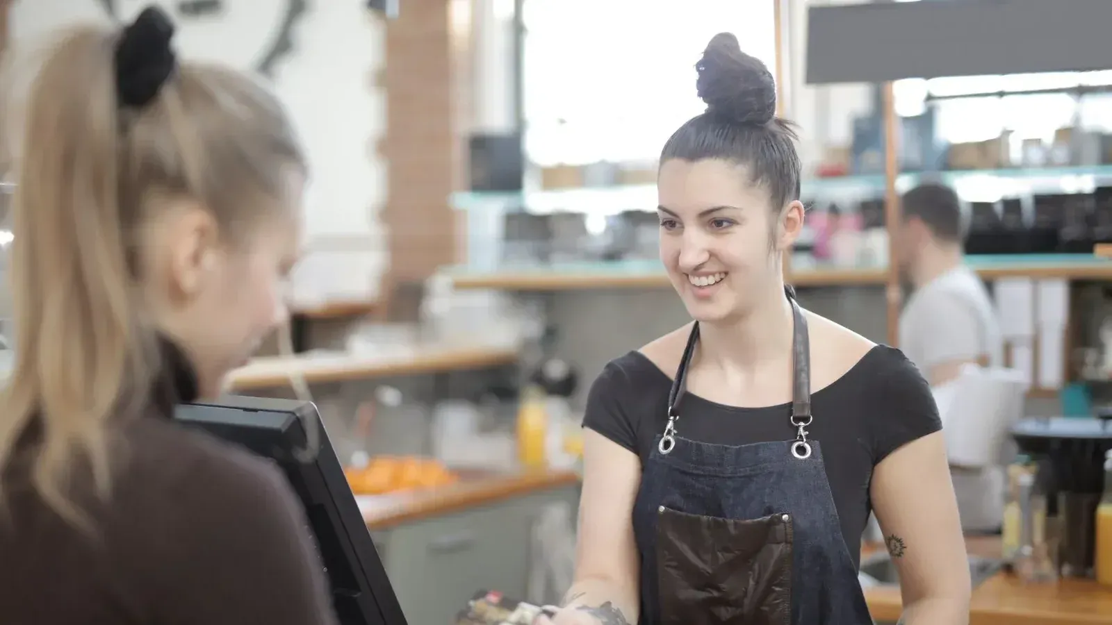 Barista in apron accepting a customer's digital payment in a cozy cafe setting.