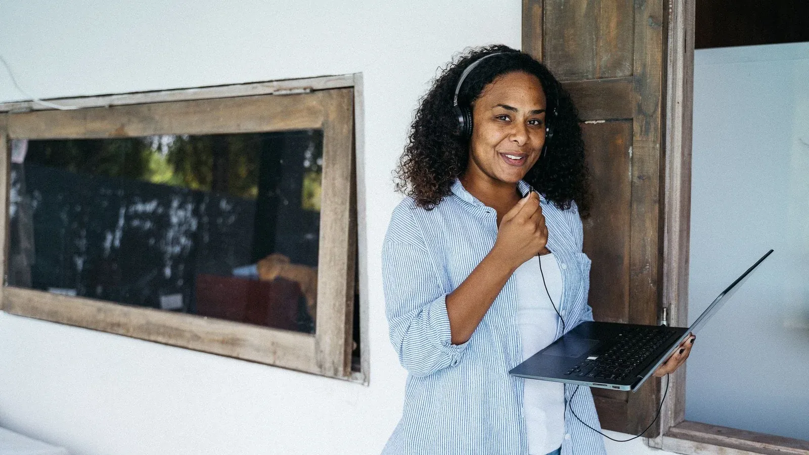 A woman enjoying remote work outdoors, wearing headphones and holding a laptop.