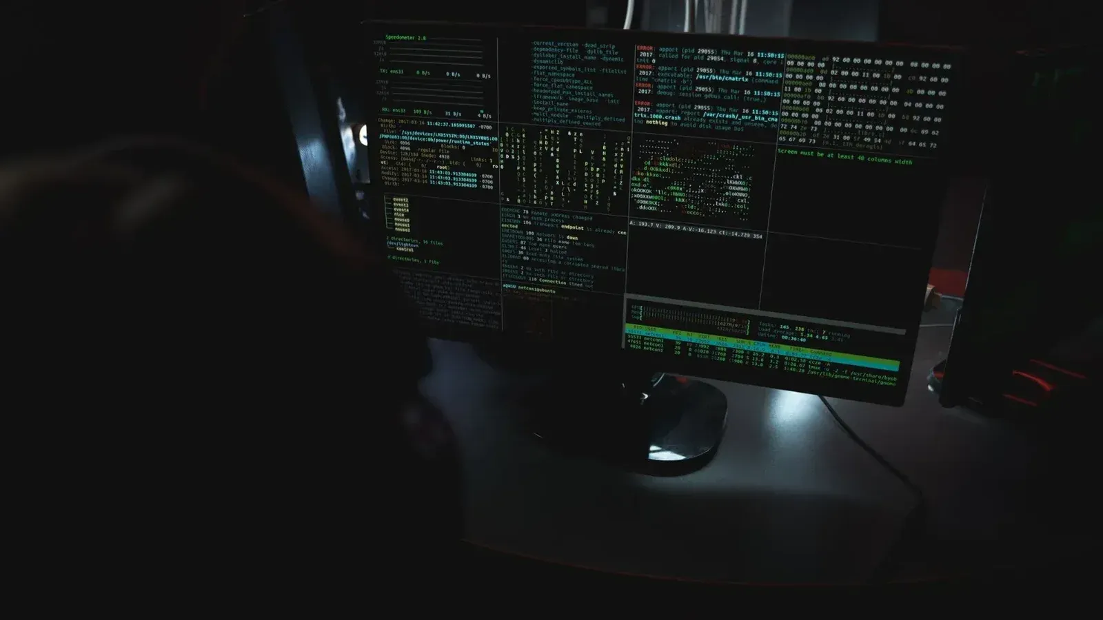 Dark room setup with code displayed on PC monitors highlighting cybersecurity themes.