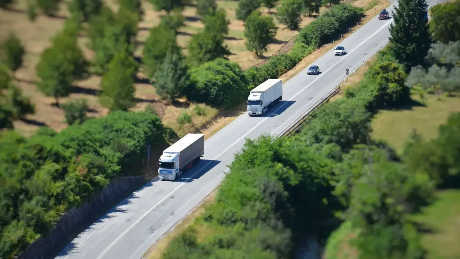 Aerial shot of a highway with trucks and cars surrounded by lush greenery.