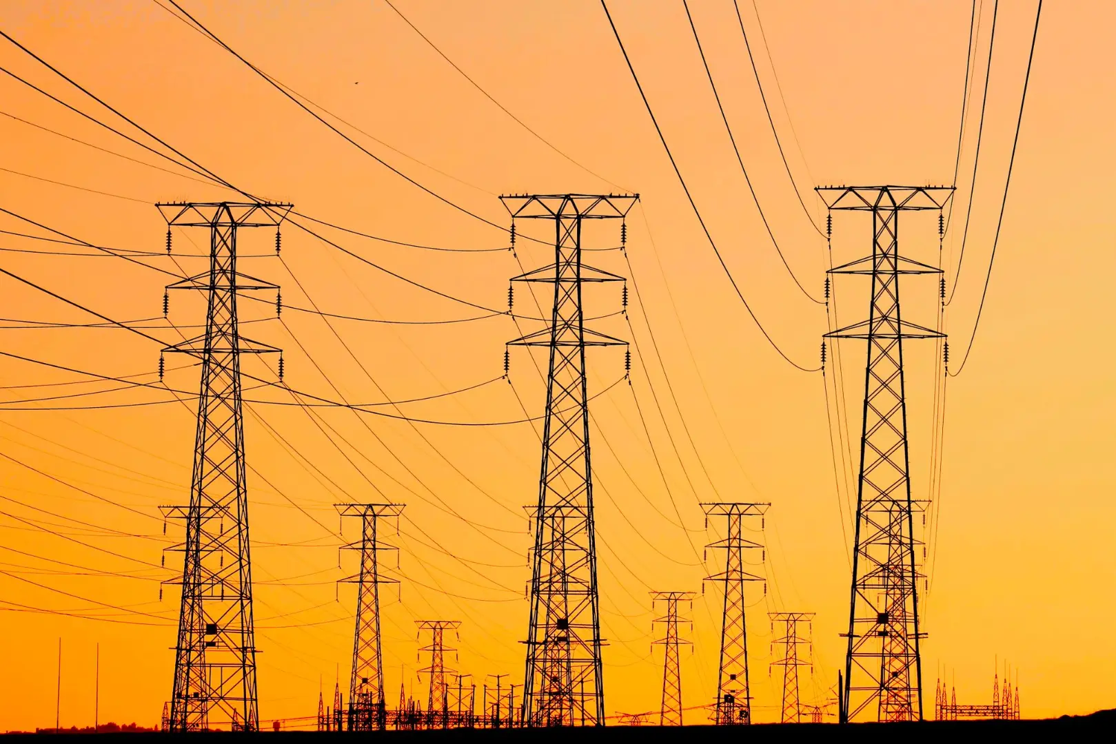 Silhouetted power lines against a vibrant orange sunset, symbolizing energy and infrastructure.