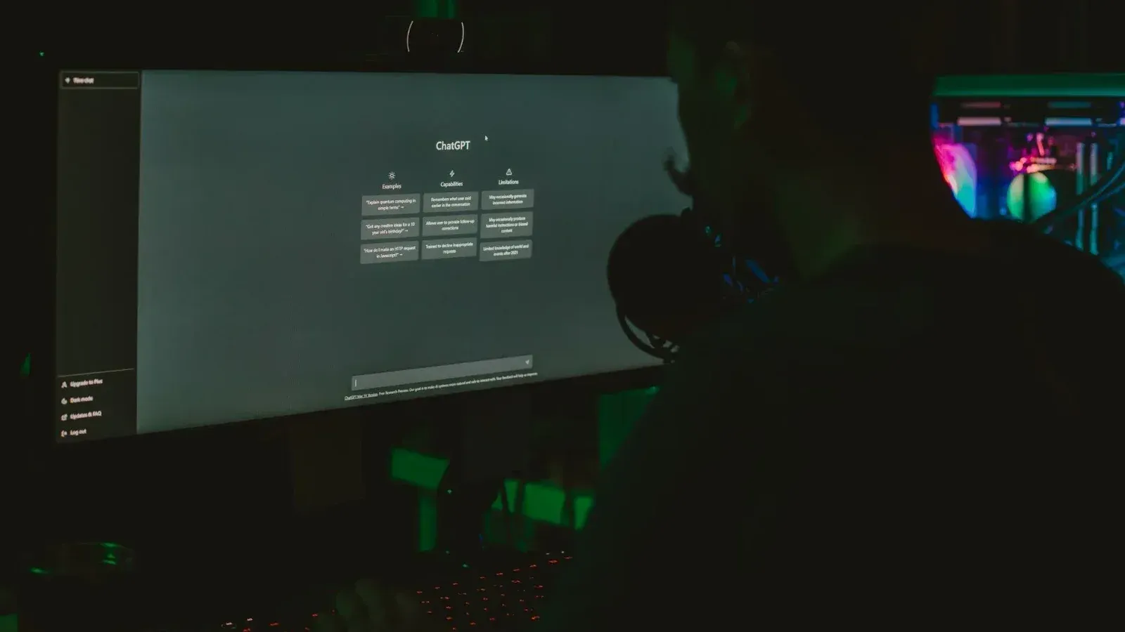 A man using a computer with a large screen in a dark room, focused on technology.