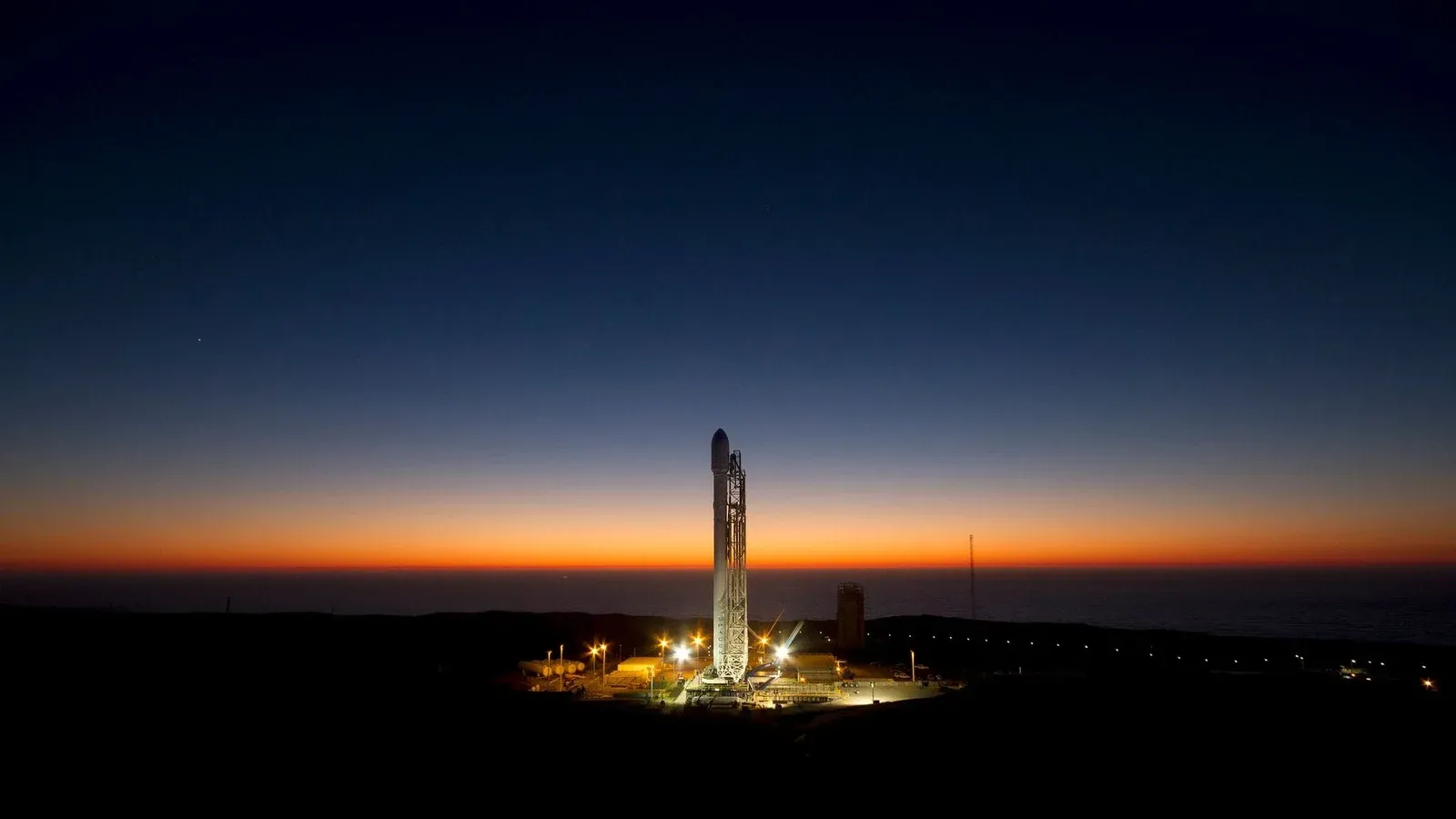 A powerful rocket stands ready on its launch pad against a stunning twilight sky.