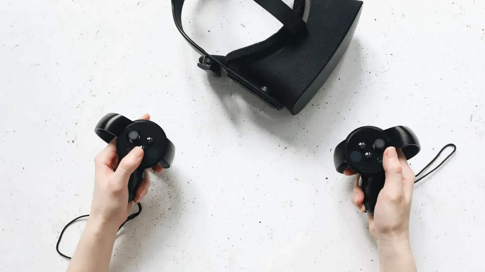 Two hands hold virtual reality controllers above a VR headset, showcasing modern technology.