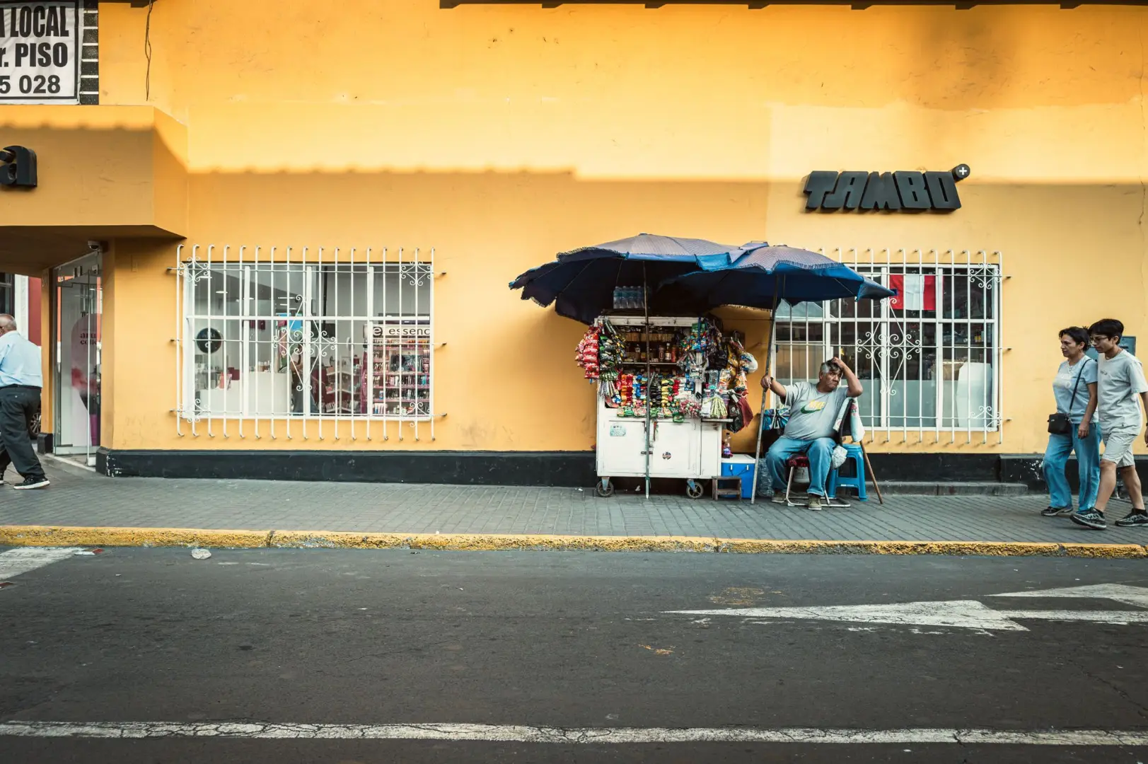 Street vendor sitting under umbrella in Trujillo with vibrant yellow wall.