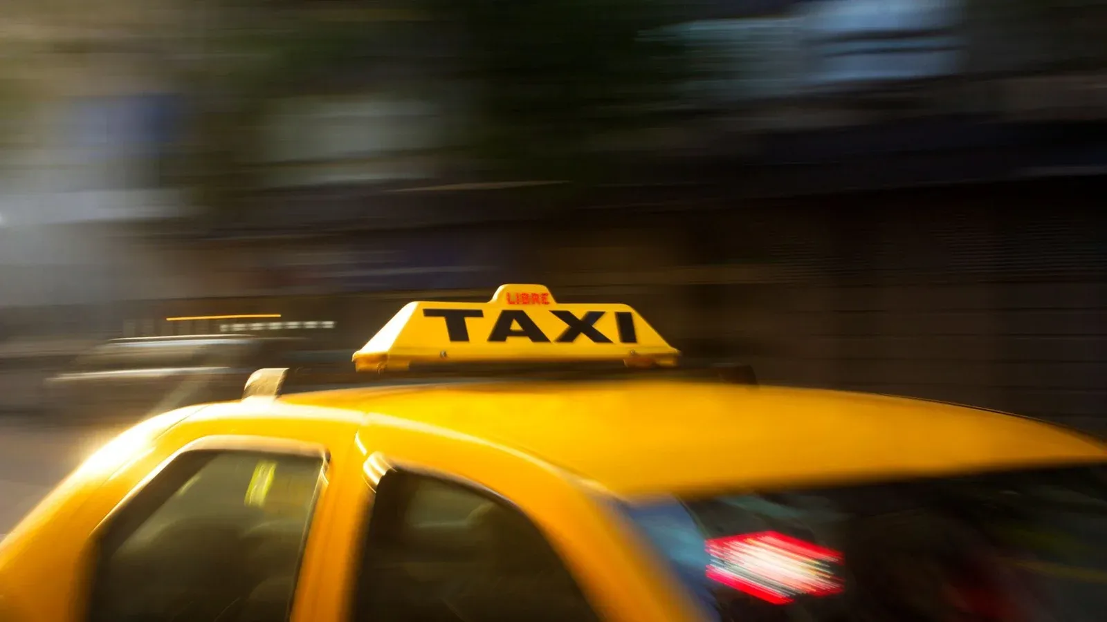 A vibrant yellow taxi with motion blur speeding through a nighttime city street.