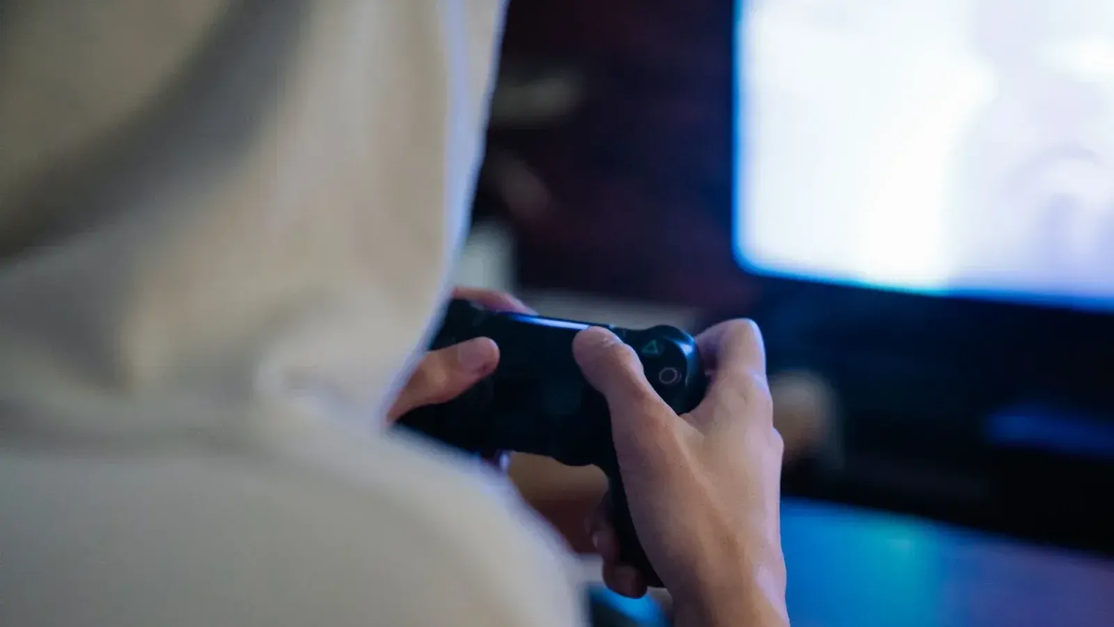 Vista posterior del hombre anónimo recortar con controlador de consola jugando videojuego contra la pantalla en casa