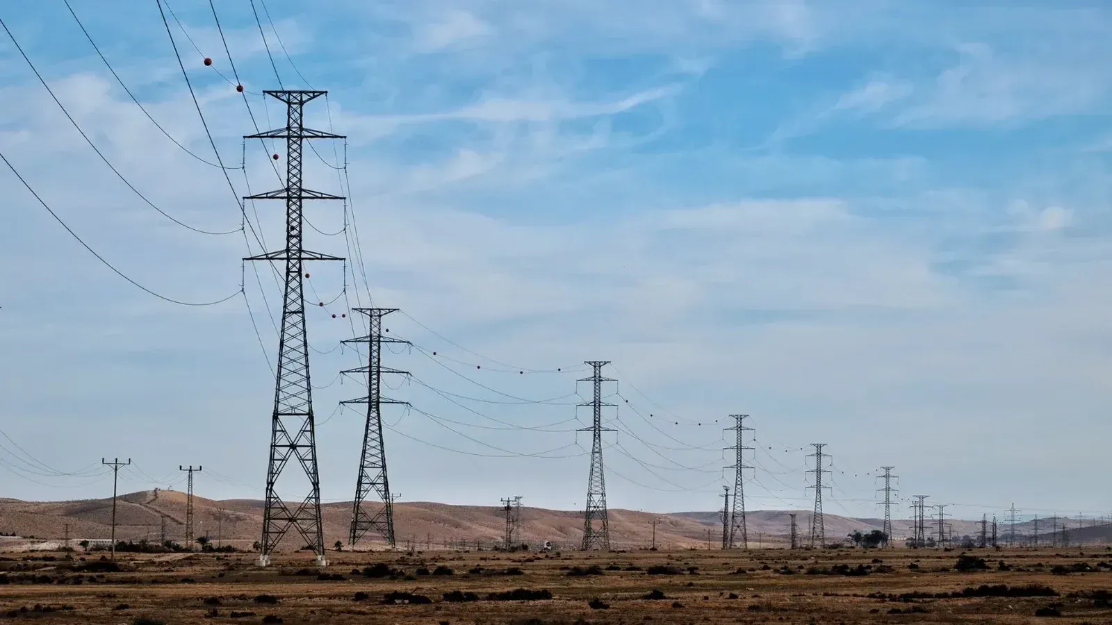 Transmission towers in a desert landscape with blue skies, showcasing energy infrastructure.
