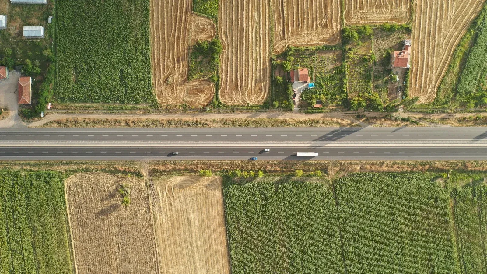 Aerial shot of a rural road cutting through lush fields, showcasing the beauty of the countryside from above.