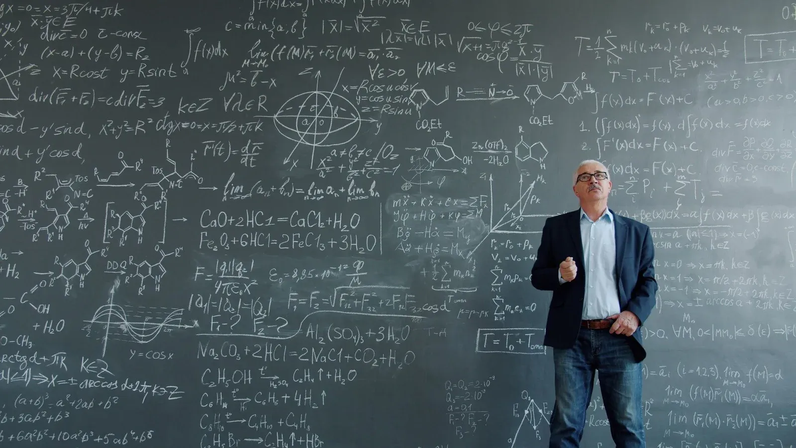 Professor standing in front of a blackboard filled with complex equations and scientific formulas.
