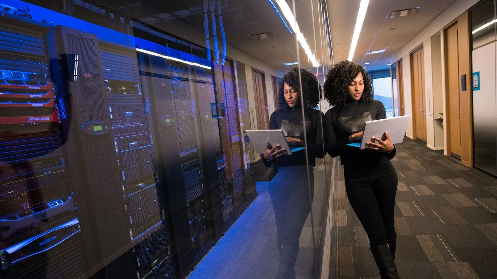 A woman using a laptop navigating a contemporary data center with mirrored servers.