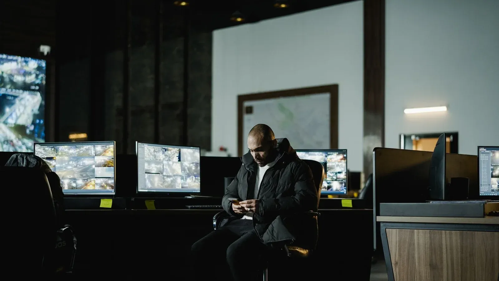 Security officer seated in a dimly lit control room, analyzing multiple surveillance screens.
